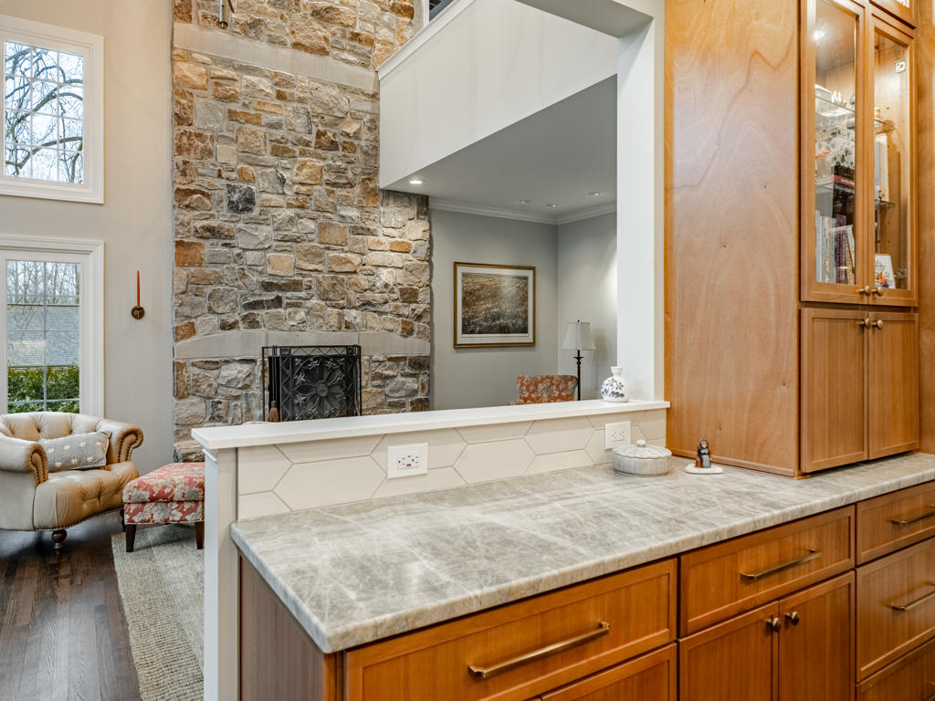 Leathered quartzite half wall counter with elongated picket tile face and view into living room featuring floor-to-ceiling Pennsylvania fieldstone fireplace