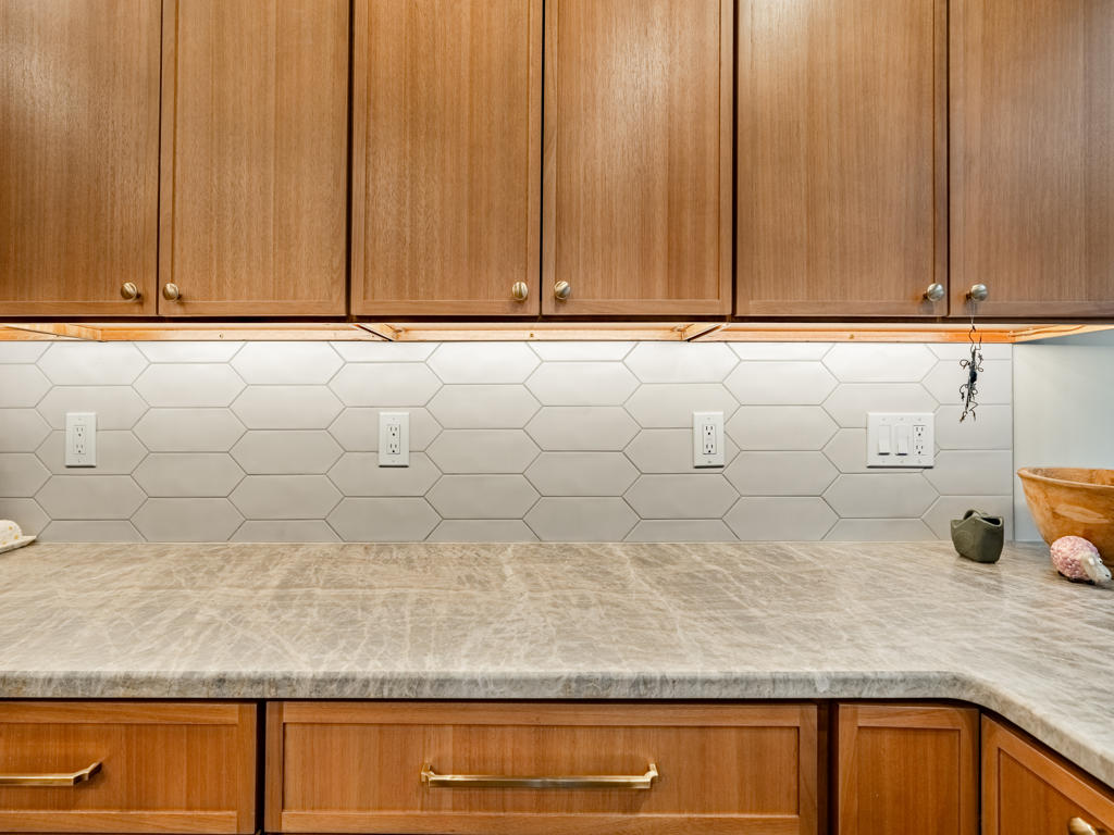 Close-up of leathered quartzite countertop with elongated picket tile backsplash and brushed bronze bar pulls on maple shaker lower cabinetry