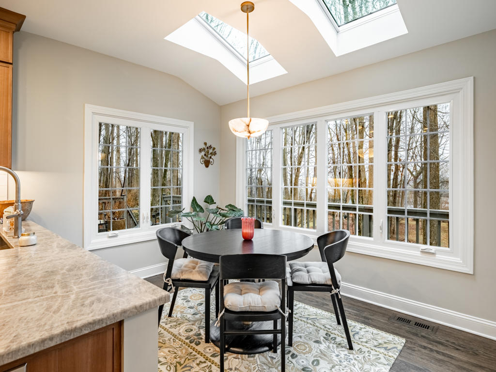Dining nook adjacent to West Chester kitchen remodel featuring twin skylights, vaulted ceiling, wraparound windows with woodland views, and stone globe pendant