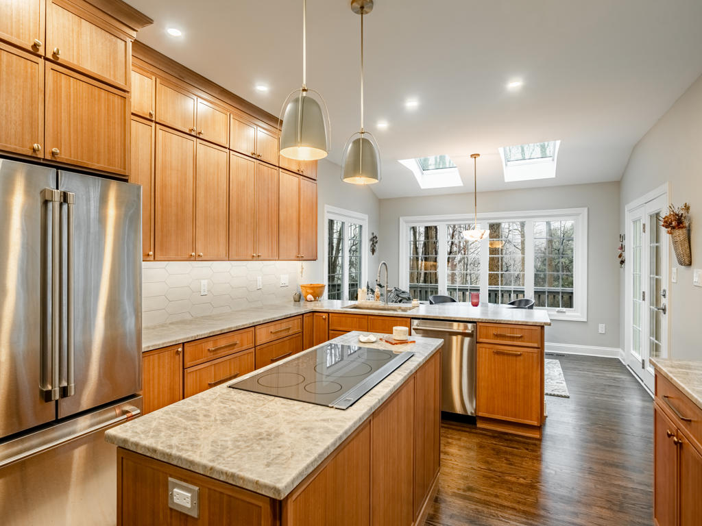 West Chester kitchen island with leathered quartzite top, dome pendants on brushed bronze stems, and full run of maple shaker cabinetry with elongated picket tile backsplash