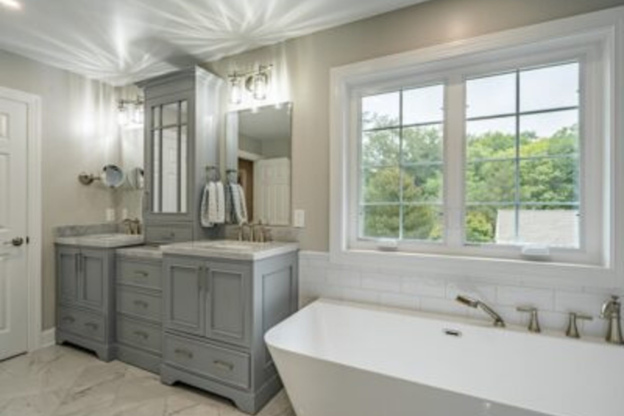 West Chester master bathroom gray vanity with freestanding soaking tub, marble floors, and large window